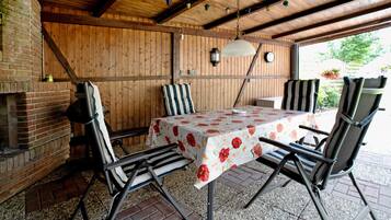 An outdoor patio with a table, chairs, a brick fireplace, and wooden walls.