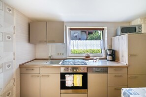 Eine kleine Küche mit Fenster, einer Mikrowelle, einer Kaffeemaschine und einem Geschirrspüler.