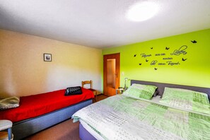 Ein Zimmer mit zwei Betten, eines mit einer roten Bettdecke und das andere mit einer grünen. An der Wand befindet sich ein Schmetterlingsaufkleber und eine Tür.