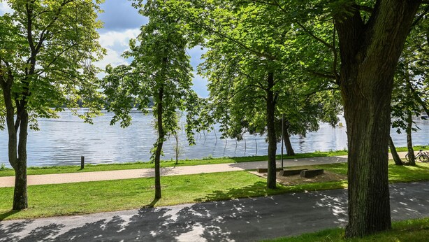 A park with a paved path, trees, and a body of water. - Apartment 'Familie Perlik' with Wi-Fi (Röbel)