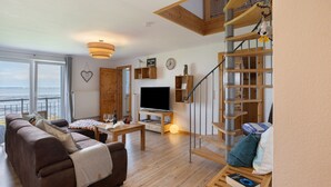Ein großzügiger Wohnbereich mit einer Couch, einem Fernseher, Holzregalen und einer Treppe.