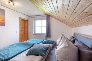 A bedroom with a sloped ceiling, a window with curtains, a bed with pillows, and a wooden door.