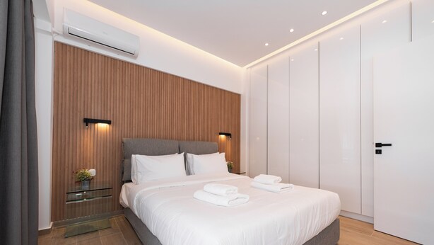 A modern bedroom with a large bed, wooden panel wall, and built-in wardrobe. - Stylish 1-Bedroom in the center, 4mins walk to Syntagma Square (Athens)
