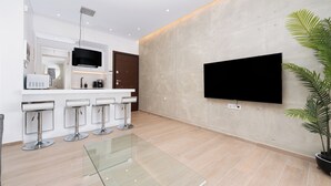 A modern kitchen with a flat-screen TV, white bar stools, and a glass dining table. - Stylish 1-Bedroom in the center, 4mins walk to Syntagma Square (Athens)