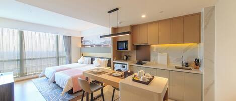 Una habitación de hotel moderna con una cama, un escritorio, una kitchenette y un gran ventanal con cortinas.