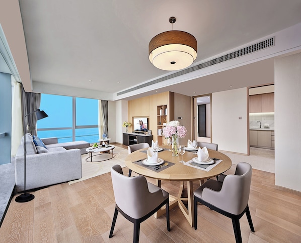 A modern hotel room with a dining area, a living area with a sofa, and a view of the sea.