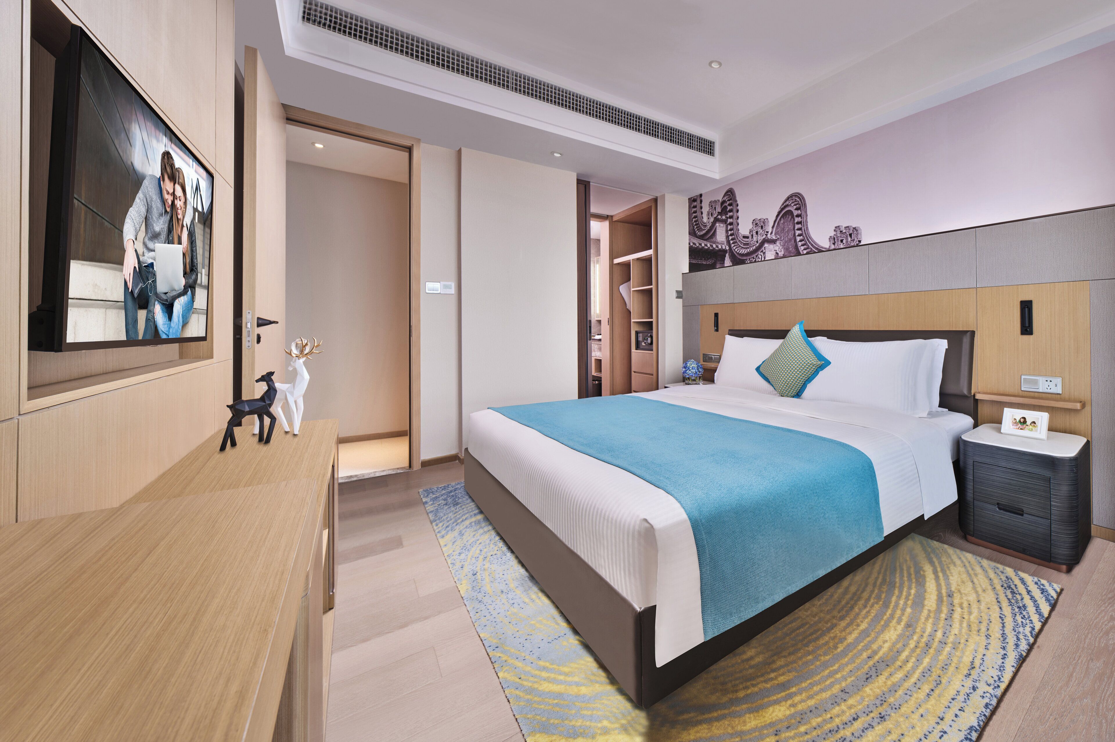 A modern hotel room with a large bed, a desk, a TV, and a wardrobe.