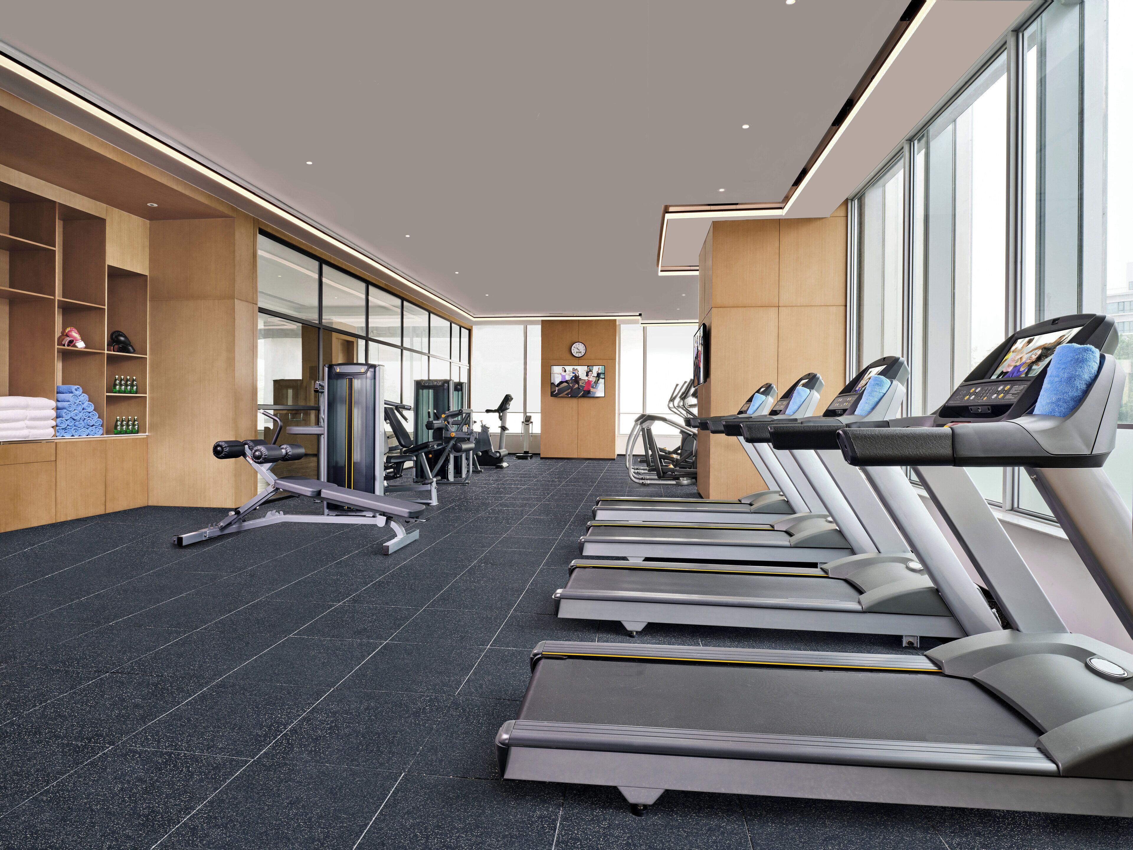 Une salle de sport moderne équipée de tapis de course, d’appareils de musculation et d’un grand mur miroir.