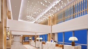 Eine moderne Hotelhalle mit Marmor-Rezeptionstheken, einer hohen Decke mit hängenden Leuchten und großen Fenstern mit Blick auf die Stadt.