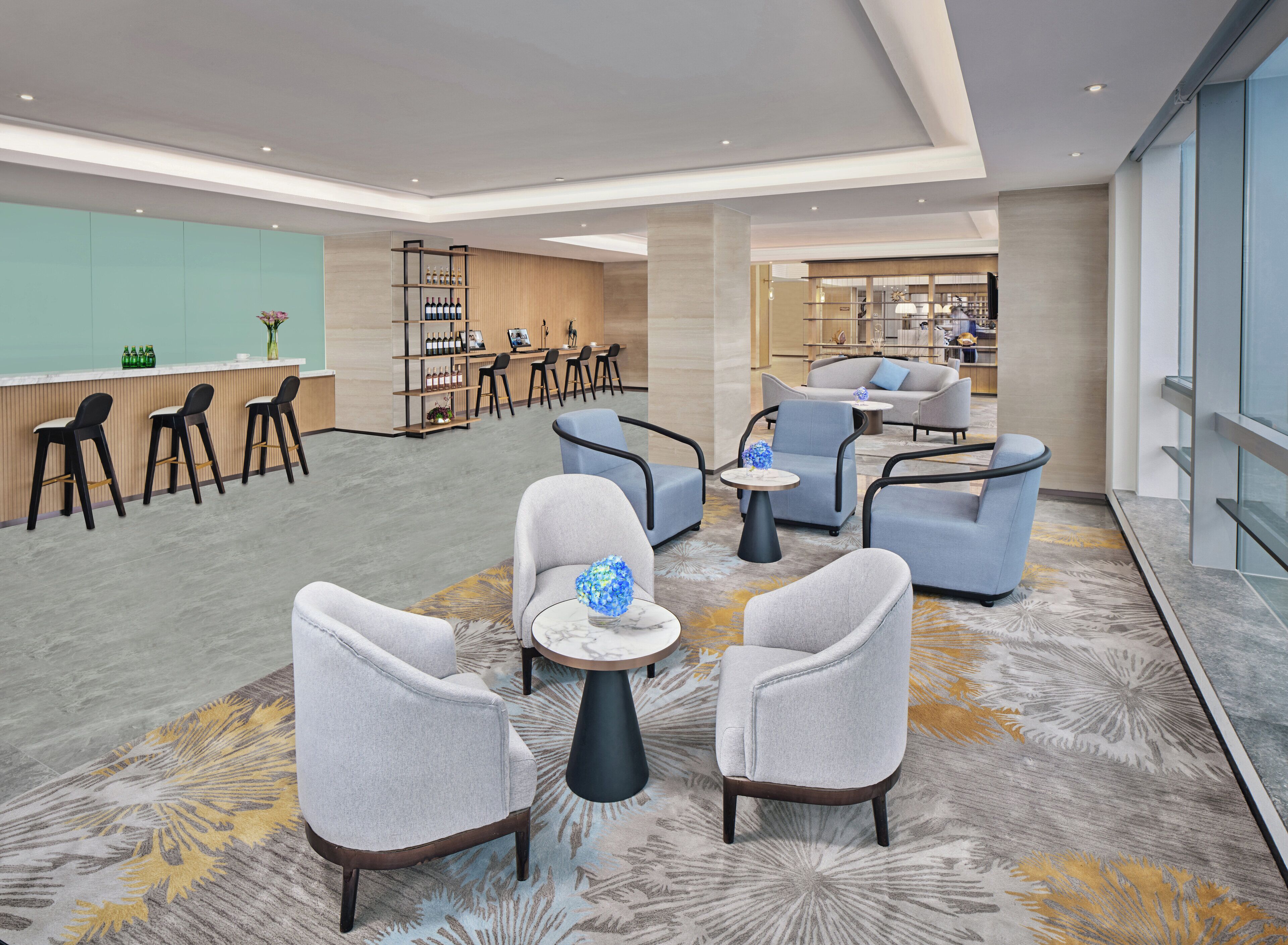 Un hall d’hôtel moderne, doté d’espaces aménagés avec des sièges, d’un bar et d’un comptoir de réception.