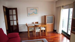 Un salon avec une table à manger en bois, deux chaises, un canapé rouge, un téléviseur et une fenêtre avec des rideaux.