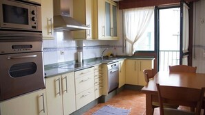 Une cuisine compacte dotée d’appareils électroménagers intégrés, un coin repas et une fenêtre avec des rideaux.
