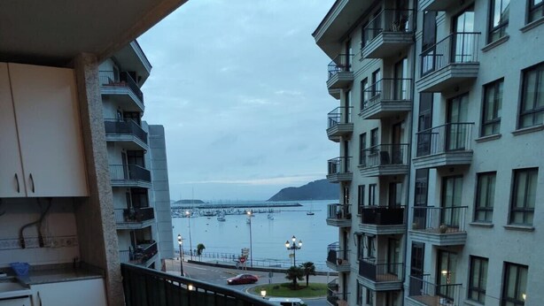 Un balcon avec une table dressée pour deux personnes, donnant sur une marina où sont amarrés des bateaux, et offrant une vue lointaine sur la mer.