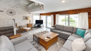 Ein geräumiges Wohnzimmer mit hoher Decke, einem Fernseher, einer Sofagarnitur und einem Holztisch.
