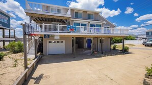 Ein zweistöckiges Strandhaus mit überdachter Veranda, Garage und Balkon mit Meerblick.