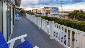 Eine Holzterrasse mit weißen Geländern, blauen Stühlen und Blick auf Strand und Meer.