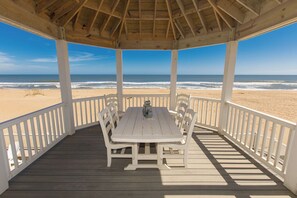 Relax in a covered outdoor seating area with a table and six chairs, taking in the breathtaking view of the beach and ocean.