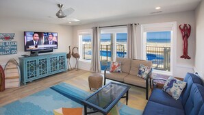 A living room with a television, a sofa, a coffee table, and a view of the beach.