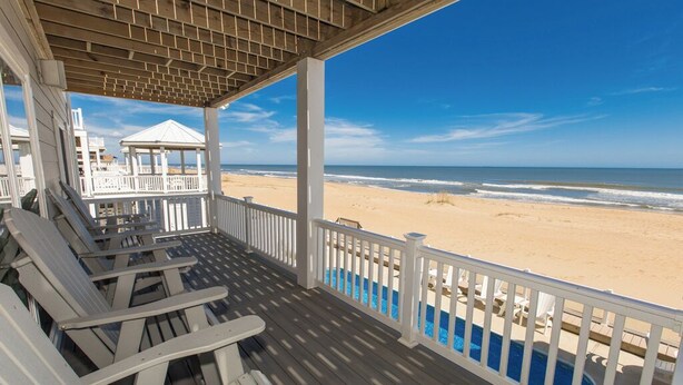 A beachside porch with wooden chairs and a view of the ocean.