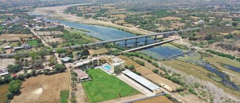 An aerial view of a town with a prominent bridge, green fields, and a large building with a swimming pool.