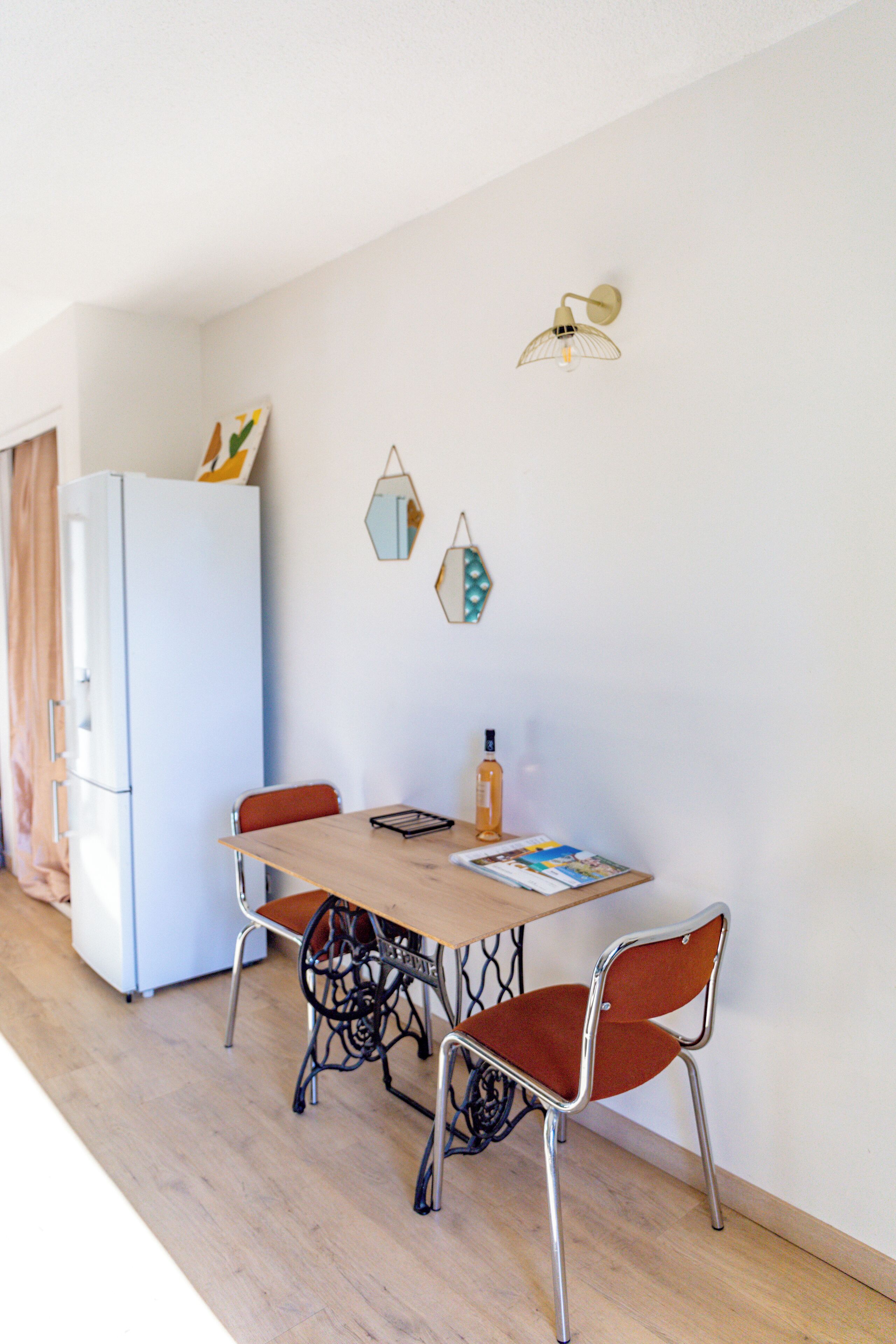 A dining area with a table, chairs, a refrigerator, and wall-mounted decor.