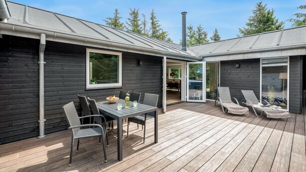 A modern outdoor patio with a wooden deck, a dining table with chairs, and a lounge area with chairs. - "Baggi" - 900m from the sea by Interhome (Blåvand)