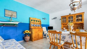 Ein Zimmer mit blauer Wand, Holzmöbeln, einem Esstisch und einem Bett mit floralem Überwurf.