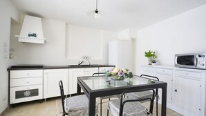 A modern kitchen with white cabinets, a black countertop, a glass dining table, and a microwave.
