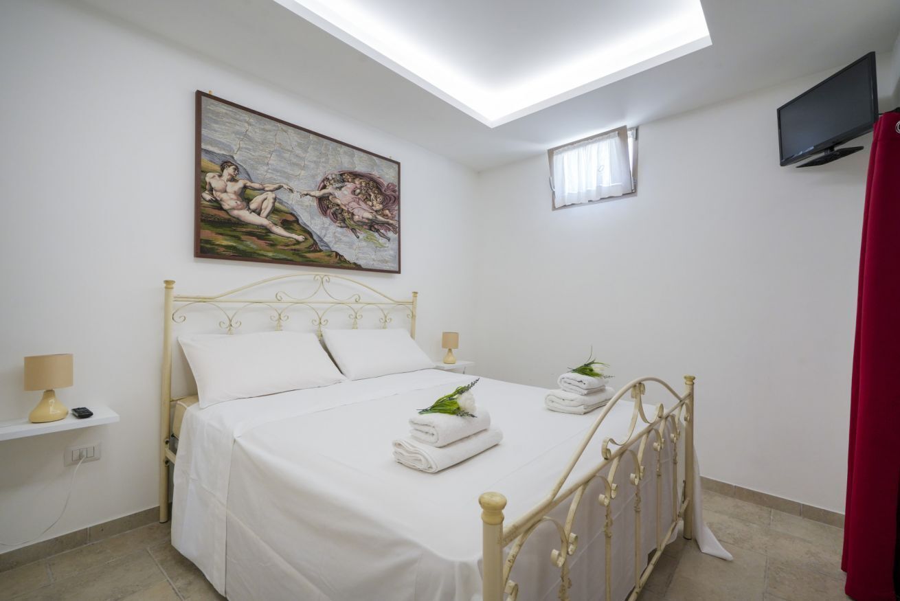 A bedroom with a bed, a painting, a TV, and a small window.