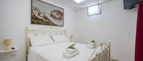 A bedroom with a bed, a painting, a TV, and a small window.