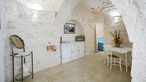 A room with a white stone wall, a white cabinet, a small table with a chair, and a decorative vase.
