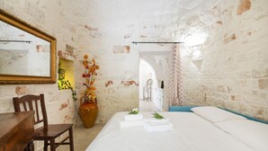 A bedroom with a bed, a wooden desk, a chair, a mirror, and a vase with flowers.