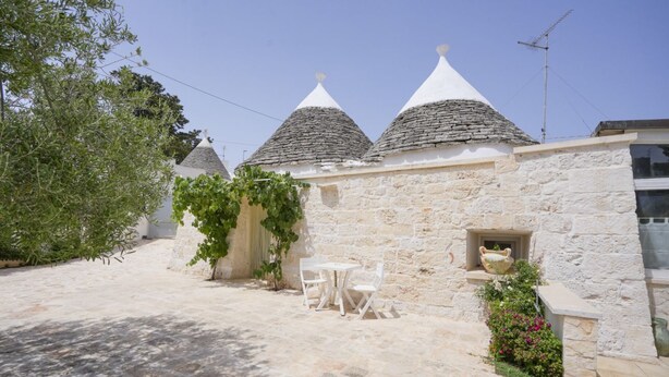 A stone building with conical roofs, a small table with chairs, and a potted plant.