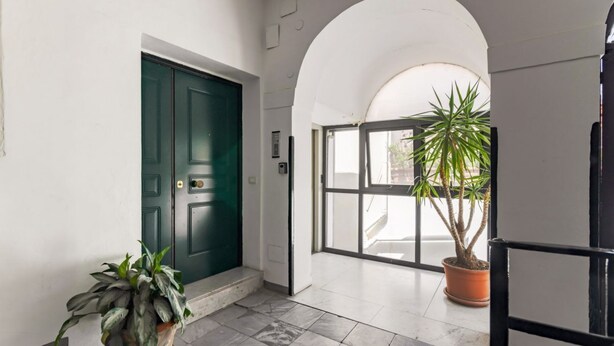 A hallway with a green door, a potted plant, and a large window with a view. - GuestHost - Palermo's Rooftop - Apt with Panoramic Terrace (Palermo)
