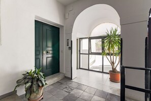 Un pasillo con una puerta verde, una planta en maceta y un ventanal con vistas.