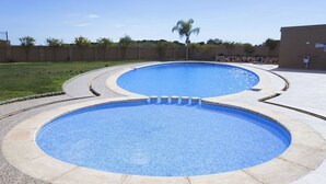A swimming pool with two distinct sections, surrounded by a tiled deck and a low brick wall.