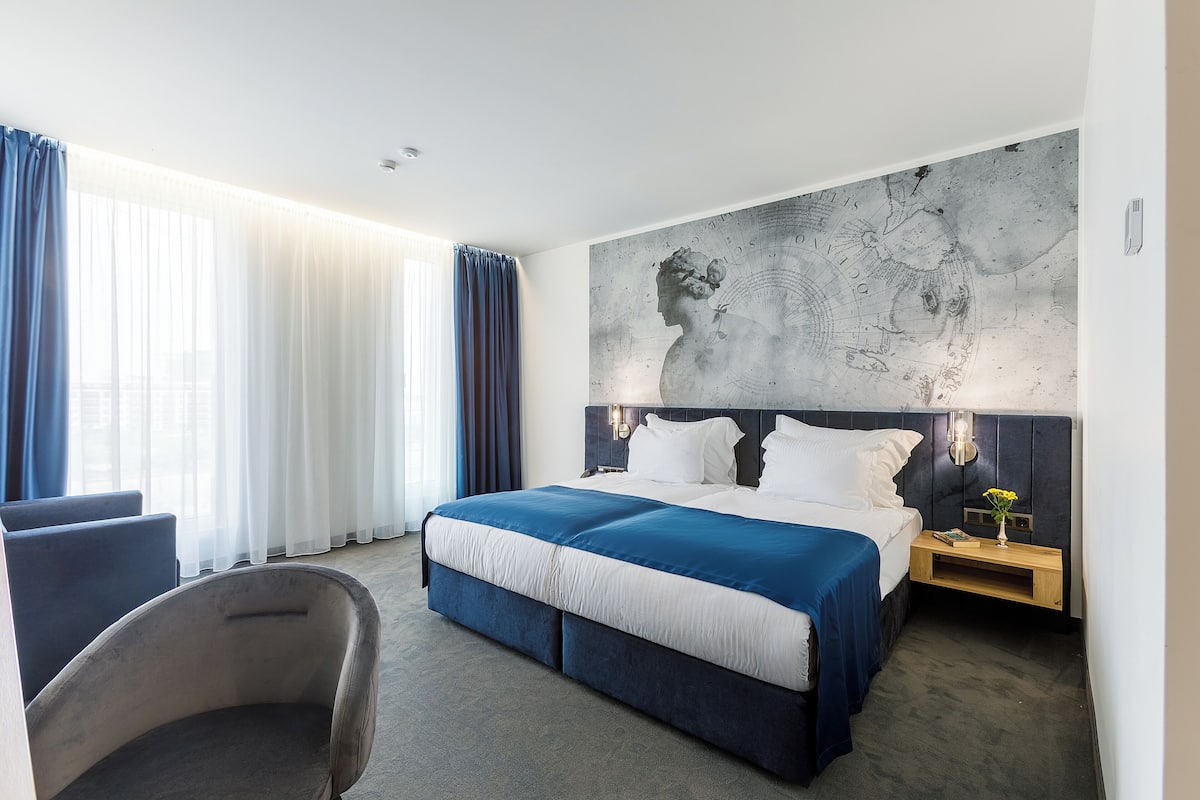 A modern hotel room with a large bed, a desk, and a chair.