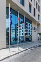 Un hotel con fachada de vidrio moderna, varias banderas y vista despejada de coches estacionados afuera.