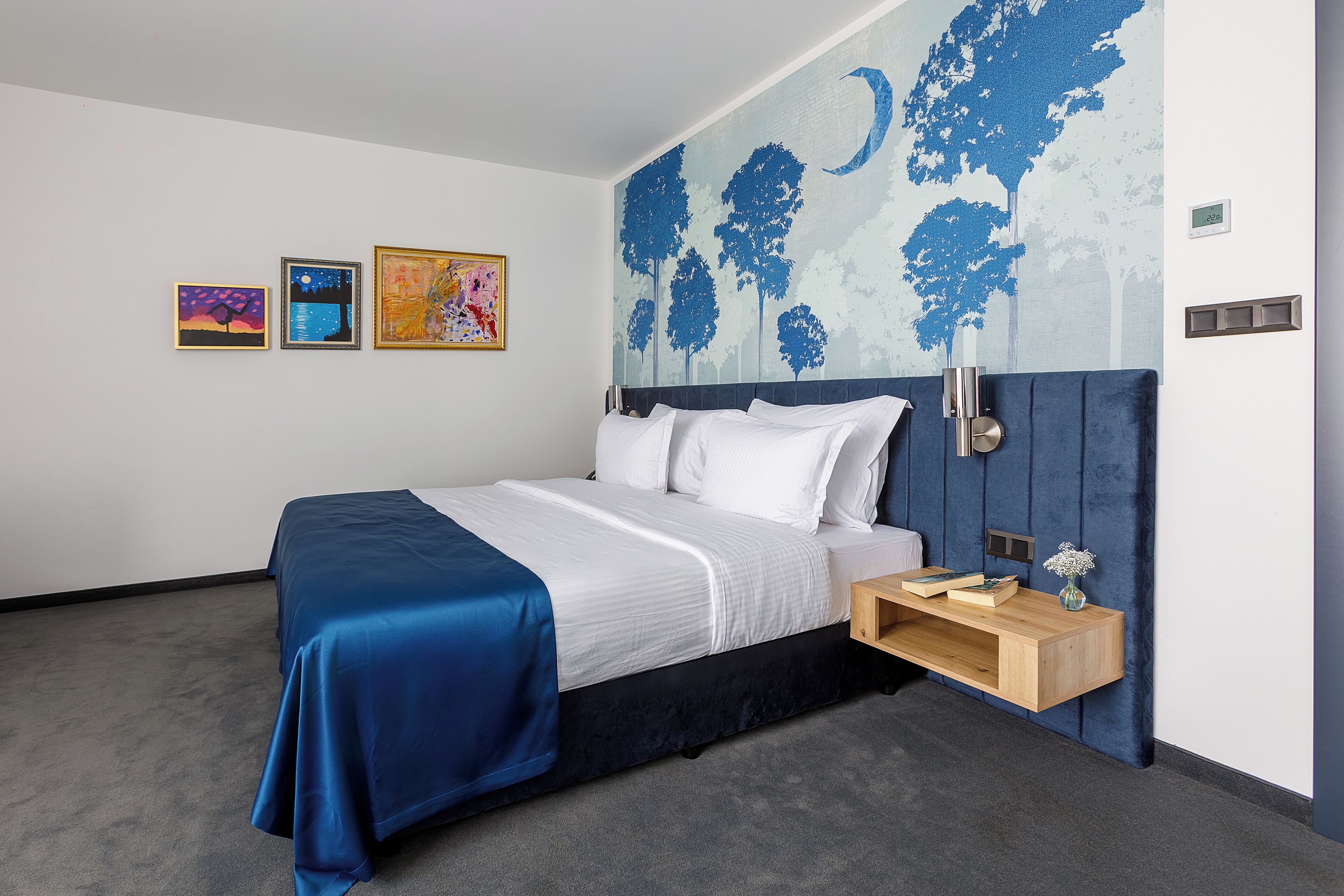 A modern hotel room with a large bed, a nightstand, and a wall mural.