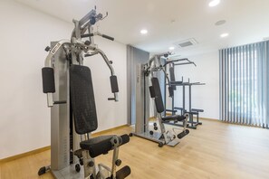 Ein Fitnessraum mit Kraftgeräten, einem Spiegel und großen Fenstern mit Vorhängen.