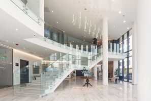 A spacious lobby with a glass staircase, marble flooring, and modern lighting fixtures.