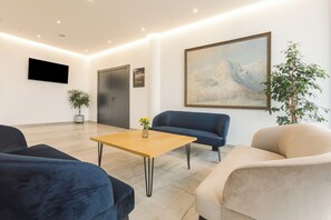 Eine moderne Lobby mit einem Holztisch, blau- und beigetonierten Sofas, einer Topfpflanze, einem Gemälde und einem Flachbildfernseher an der Wand.