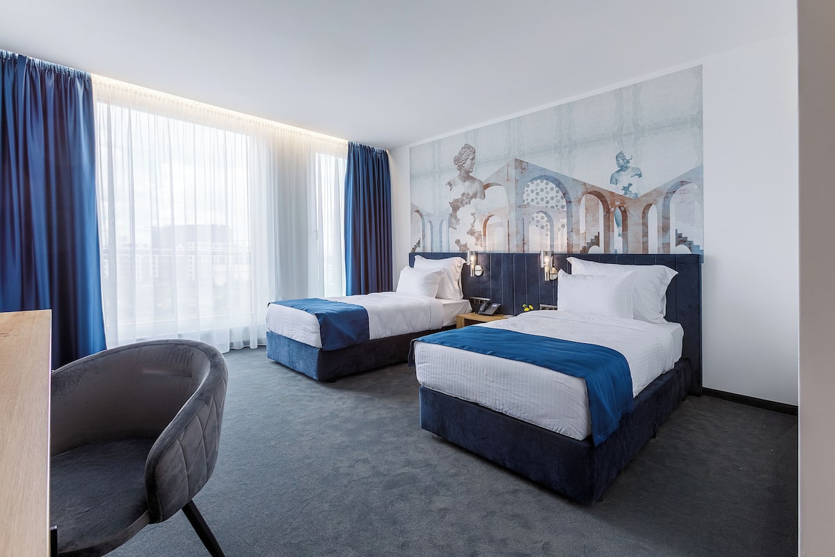 A hotel room with two beds, a chair, and a large window with curtains.