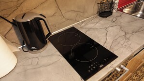 A kitchen with a black induction cooktop, a black kettle, and a marble countertop.