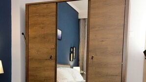 A bedroom with a bed, a wooden wardrobe, and a mirror reflecting the room.