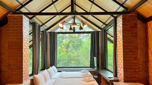 Ein Zimmer mit einem Bett, einer Bank und einem Fenster mit Blick auf Bäume.
