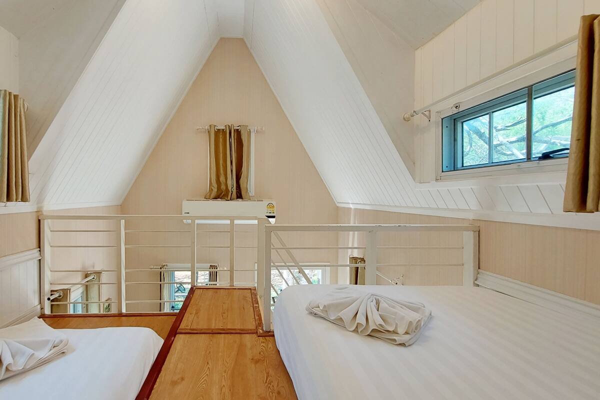 A room with two beds, a wooden floor, a window, and a ceiling with a triangular design.