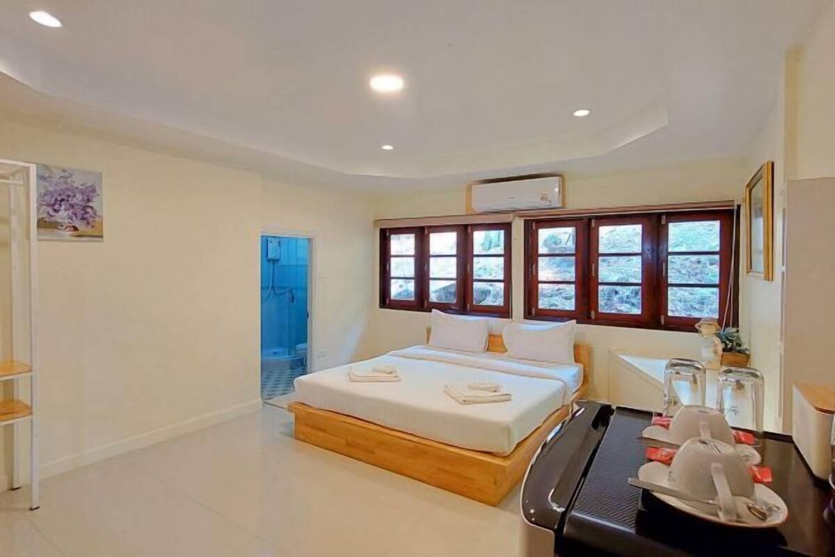 A bedroom with a bed, a desk with a chair, a window with a view, and a door leading to another room.