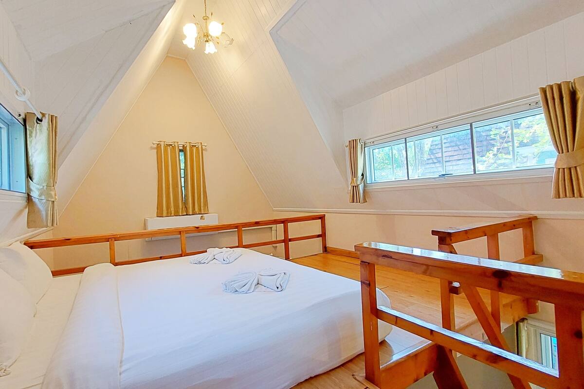 A bedroom with a bed, wooden headboard, a window with curtains, and a ceiling light fixture.