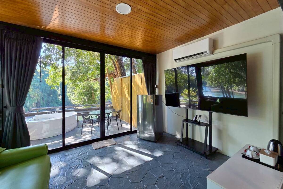 A modern room with a large window, a flat-screen TV, a sofa, and a table with a kettle.